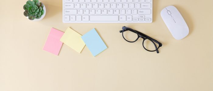 Office workplace table with computer keyboard, mouse, glasses, blank stickers and plant top view